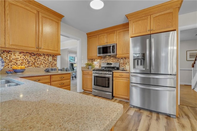 kitchen featuring light wood-type flooring, appliances with stainless steel finishes, backsplash, and light stone counters