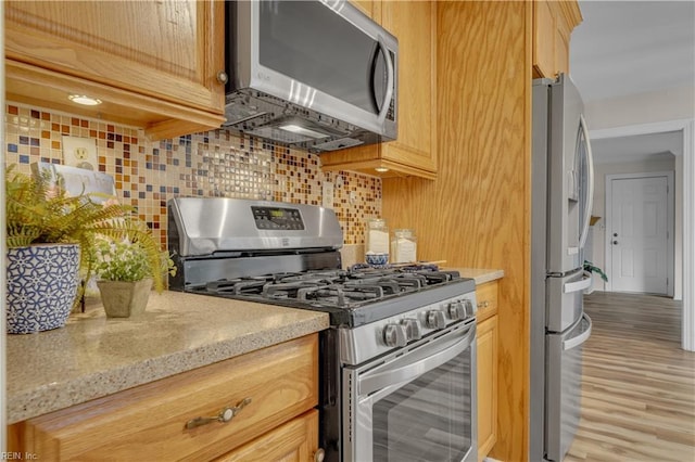 kitchen featuring light brown cabinets, light hardwood / wood-style flooring, decorative backsplash, light stone counters, and stainless steel appliances