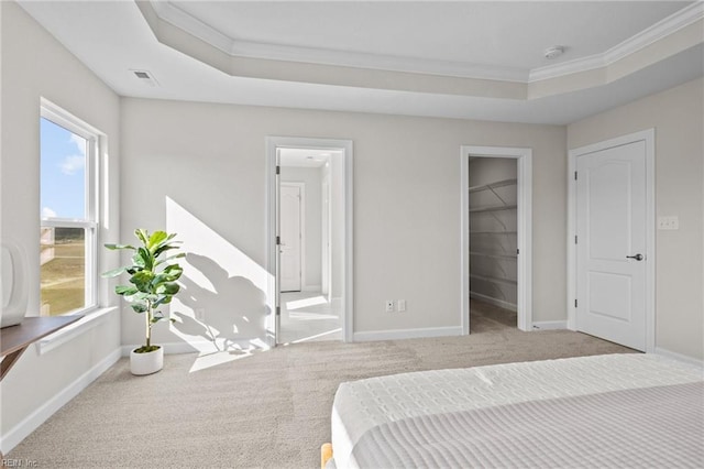 carpeted bedroom with a tray ceiling, a walk in closet, and crown molding