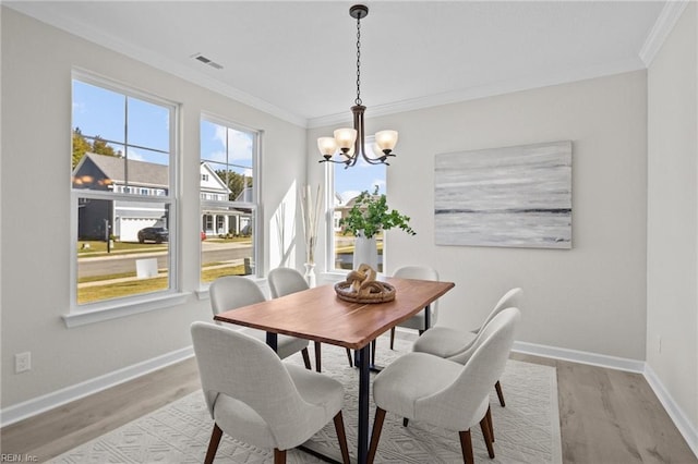 dining space with light wood-type flooring, ornamental molding, and a notable chandelier