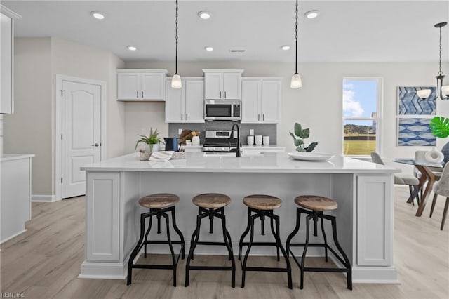 kitchen with a large island, stainless steel appliances, hanging light fixtures, and light hardwood / wood-style flooring