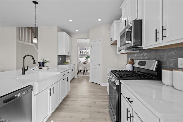 kitchen featuring white cabinets, light stone countertops, light wood-type flooring, decorative light fixtures, and stainless steel appliances