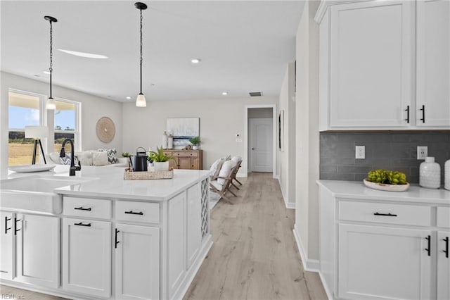 kitchen featuring white cabinets, sink, hanging light fixtures, light hardwood / wood-style flooring, and tasteful backsplash