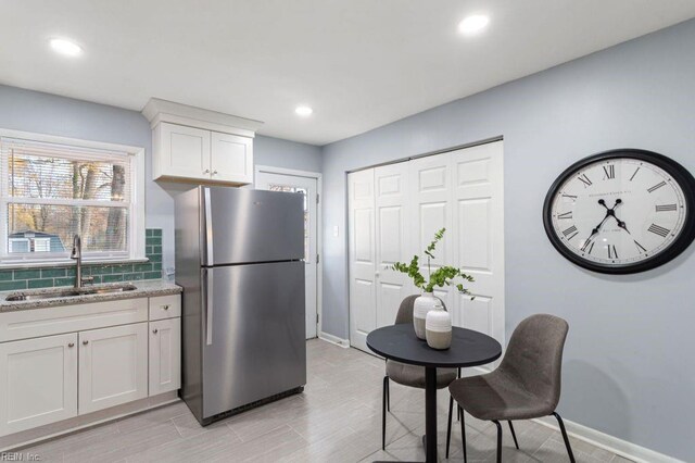 kitchen featuring stainless steel refrigerator, light stone countertops, sink, light hardwood / wood-style floors, and white cabinets