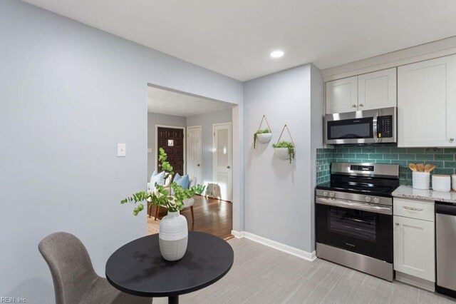 kitchen with white cabinets, light stone counters, backsplash, and appliances with stainless steel finishes