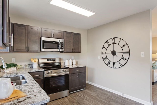 kitchen featuring sink, light stone countertops, appliances with stainless steel finishes, dark brown cabinets, and dark hardwood / wood-style flooring