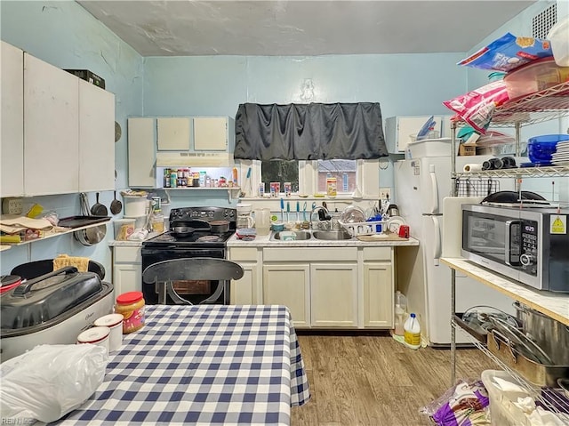 kitchen with light wood-type flooring, black range with electric cooktop, white cabinets, and sink