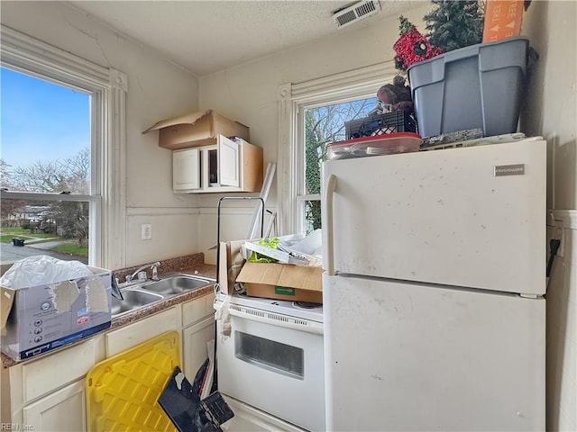 kitchen with white cabinets, a textured ceiling, white refrigerator, and sink