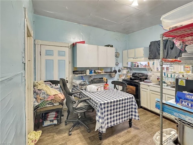 kitchen with black electric range, light wood-type flooring, white cabinetry, and sink