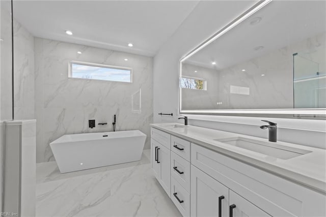 bathroom with vanity, a healthy amount of sunlight, a tub to relax in, and tile walls