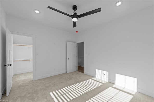 unfurnished bedroom with light carpet, a walk in closet, a closet, and ceiling fan