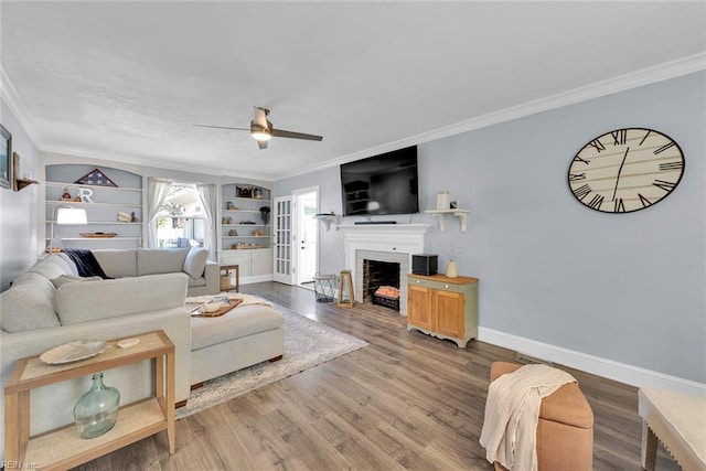 living room with built in shelves, hardwood / wood-style floors, ceiling fan, and crown molding