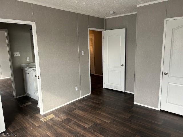 unfurnished bedroom featuring ensuite bath, dark hardwood / wood-style flooring, and a textured ceiling