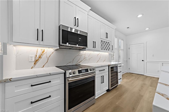 kitchen featuring light wood-type flooring, backsplash, stainless steel appliances, white cabinetry, and wine cooler