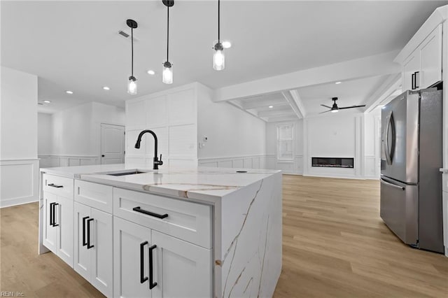 kitchen featuring stainless steel fridge, sink, white cabinetry, and an island with sink