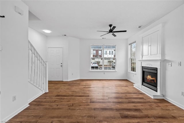 unfurnished living room featuring ceiling fan, a large fireplace, and dark wood-type flooring