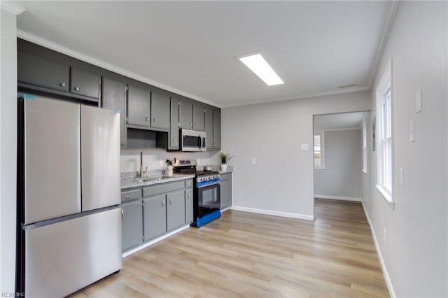 kitchen featuring sink, light stone countertops, light wood-type flooring, appliances with stainless steel finishes, and ornamental molding