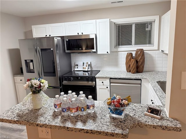 kitchen with light stone countertops, white cabinets, appliances with stainless steel finishes, tasteful backsplash, and kitchen peninsula