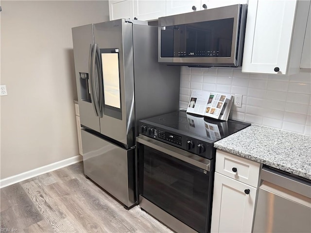 kitchen with light stone countertops, white cabinets, stainless steel appliances, and light wood-type flooring