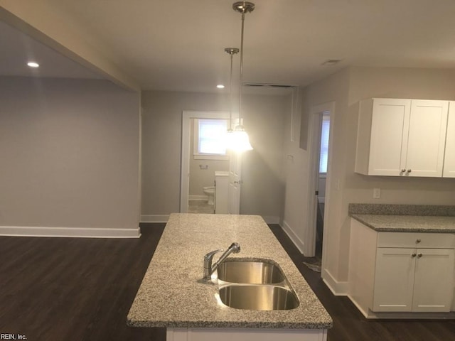 kitchen with decorative light fixtures, white cabinets, light stone counters, and sink