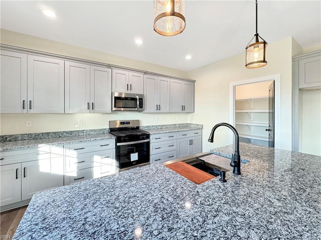 kitchen with light stone countertops, sink, hanging light fixtures, stainless steel appliances, and dark hardwood / wood-style floors