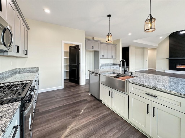 kitchen featuring sink, light stone counters, dark hardwood / wood-style flooring, decorative light fixtures, and appliances with stainless steel finishes