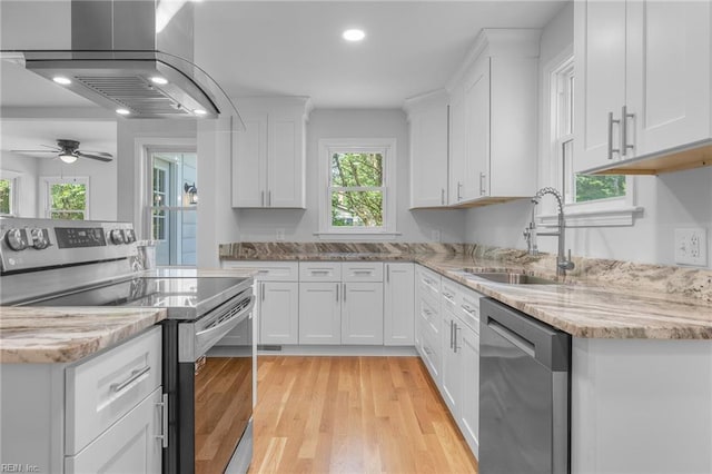 kitchen with island exhaust hood, appliances with stainless steel finishes, a wealth of natural light, sink, and white cabinets