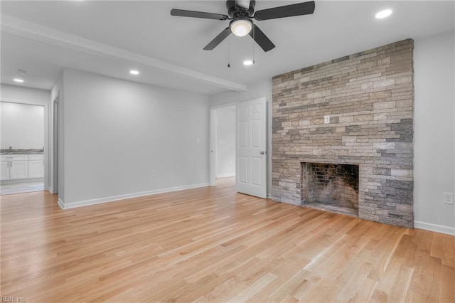 unfurnished living room with a stone fireplace, ceiling fan, and light hardwood / wood-style floors