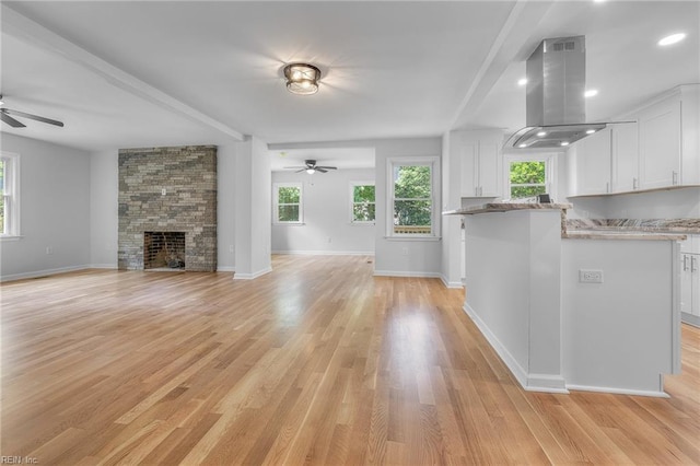 unfurnished living room featuring ceiling fan, a stone fireplace, and light hardwood / wood-style flooring