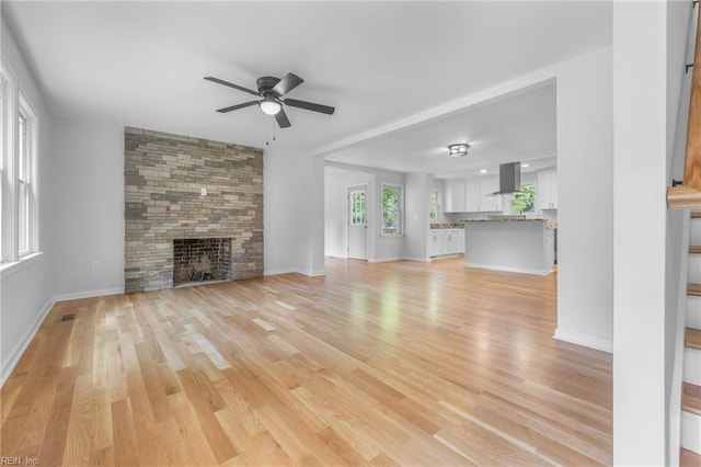 unfurnished living room with ceiling fan, a fireplace, and light hardwood / wood-style flooring