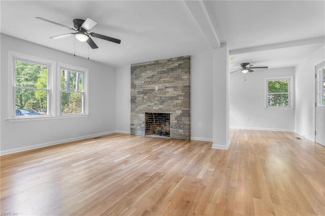 unfurnished living room with ceiling fan, a stone fireplace, and light hardwood / wood-style flooring