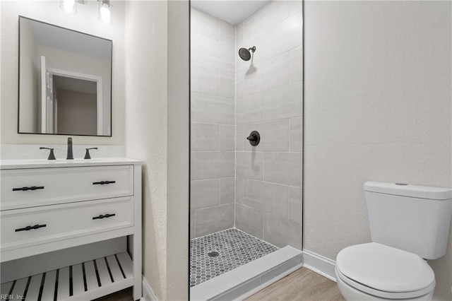 bathroom featuring tiled shower, vanity, hardwood / wood-style flooring, and toilet