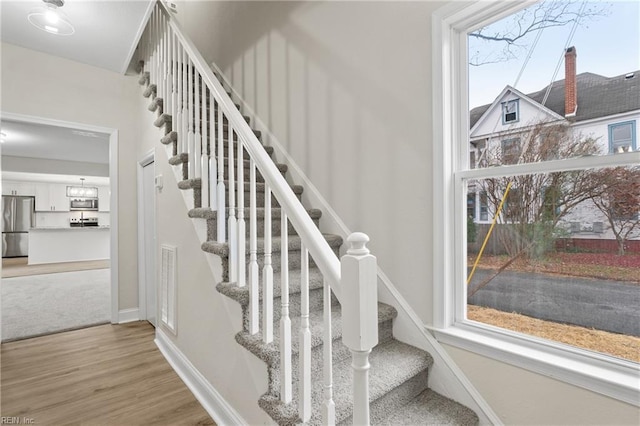 staircase with hardwood / wood-style flooring, a wealth of natural light, and a chandelier