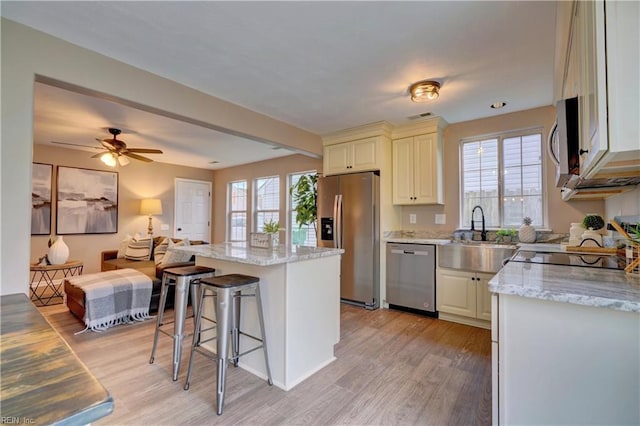 kitchen featuring light stone countertops, sink, stainless steel appliances, a kitchen island, and light wood-type flooring