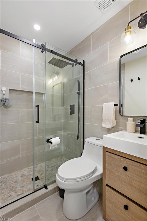 bathroom featuring vanity, tile patterned floors, toilet, tile walls, and an enclosed shower