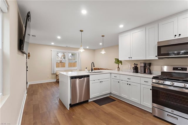 kitchen with kitchen peninsula, sink, appliances with stainless steel finishes, decorative light fixtures, and white cabinetry