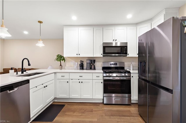 kitchen with pendant lighting, sink, hardwood / wood-style flooring, white cabinetry, and stainless steel appliances