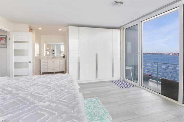 bedroom with access to exterior, floor to ceiling windows, a water view, connected bathroom, and light hardwood / wood-style floors