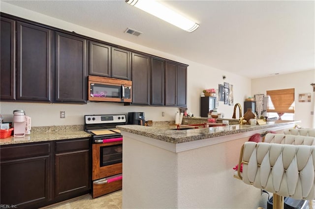 kitchen featuring light stone countertops, dark brown cabinetry, stainless steel appliances, and kitchen peninsula