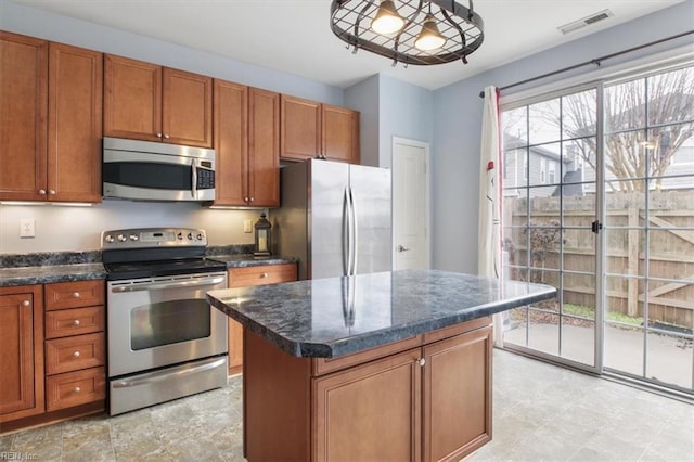 kitchen with a kitchen island, dark stone counters, decorative light fixtures, and appliances with stainless steel finishes