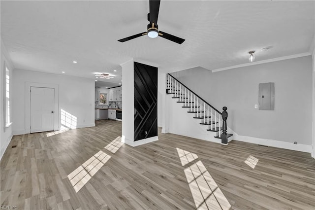 unfurnished living room featuring light wood-type flooring, ceiling fan, electric panel, and ornamental molding