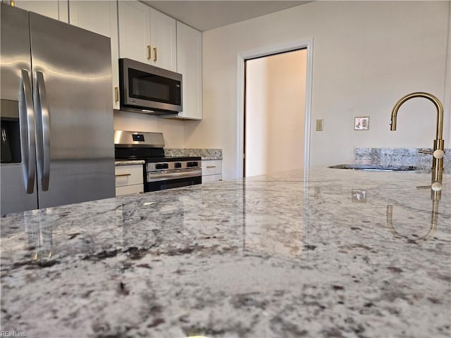 kitchen with white cabinets, stainless steel appliances, light stone counters, and sink