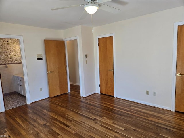 unfurnished bedroom with ensuite bathroom, ceiling fan, dark wood-type flooring, and tile walls