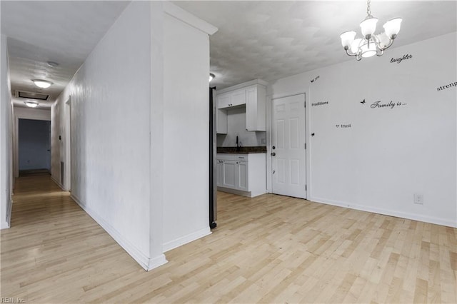 unfurnished room featuring an inviting chandelier, light hardwood / wood-style flooring, and sink