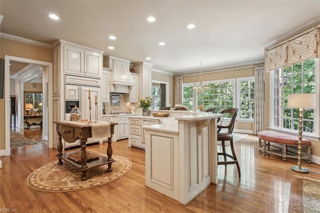 kitchen with premium range hood, a kitchen island with sink, sink, ornamental molding, and decorative light fixtures