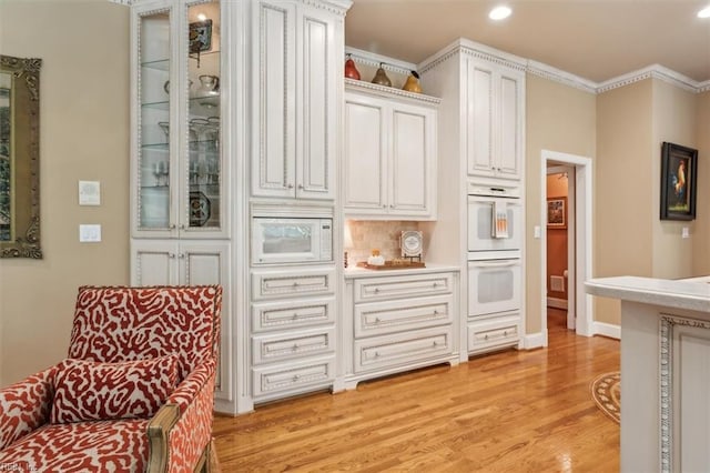 kitchen with white appliances, crown molding, light hardwood / wood-style flooring, tasteful backsplash, and white cabinetry