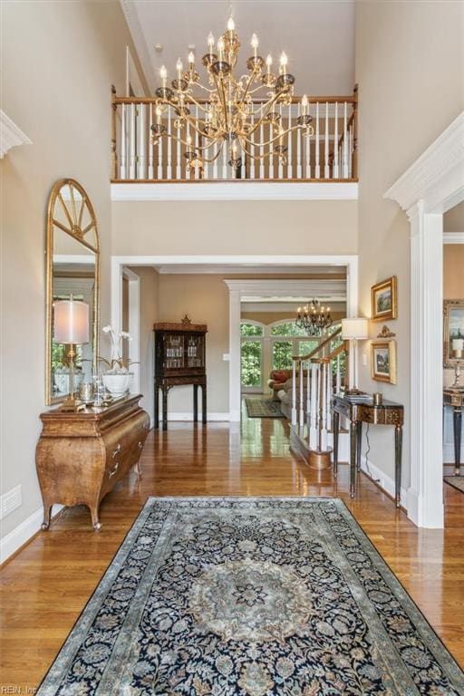 entrance foyer featuring a notable chandelier, wood-type flooring, ornamental molding, and a high ceiling