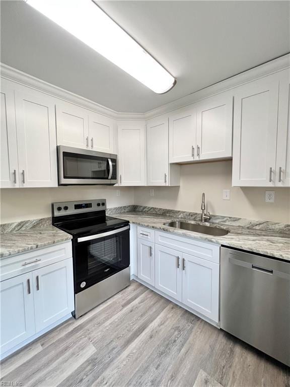 kitchen with sink, light stone countertops, appliances with stainless steel finishes, light hardwood / wood-style floors, and white cabinetry