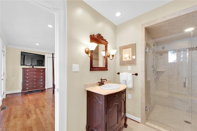 bathroom with hardwood / wood-style flooring, vanity, a shower with shower door, and ornamental molding