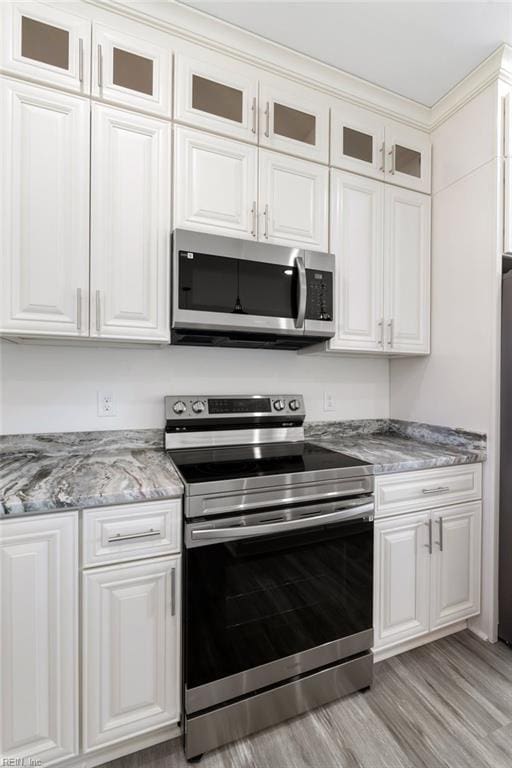 kitchen with white cabinets, light wood-type flooring, stainless steel appliances, and stone countertops